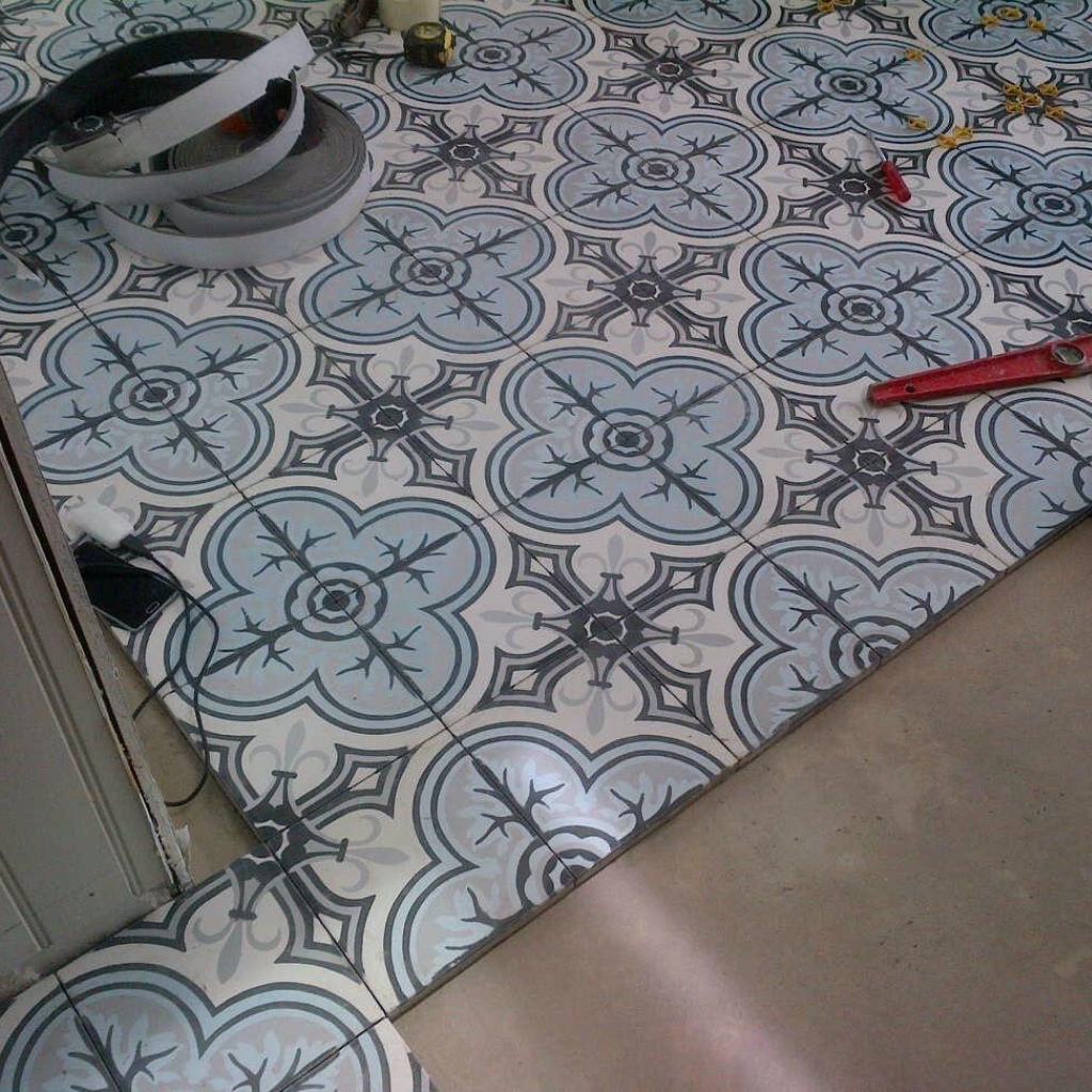 Pose en cours de carreaux de ciment à motifs bleus et noirs sur un sol intérieur.