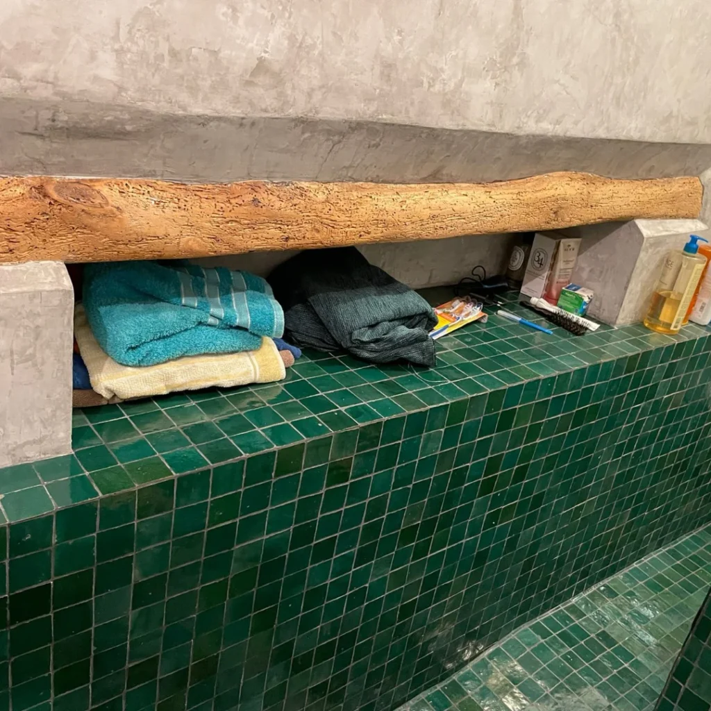 Hammam moderne avec zellige vert profond de Fès, bois brut et béton ciré.