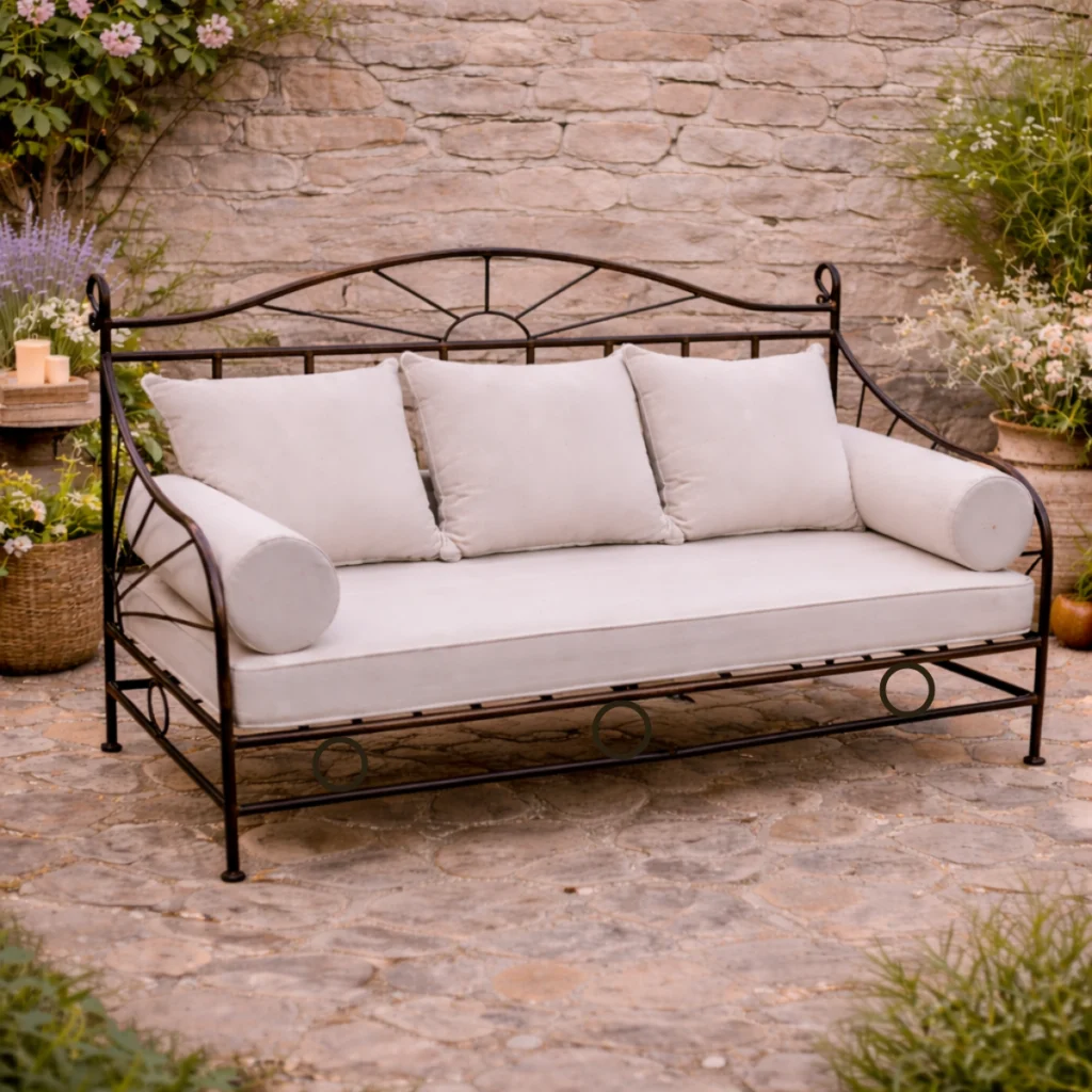 Banquette de jardin en fer forgé avec coussins blancs sur terrasse en pierre naturelle sous espace couvert.