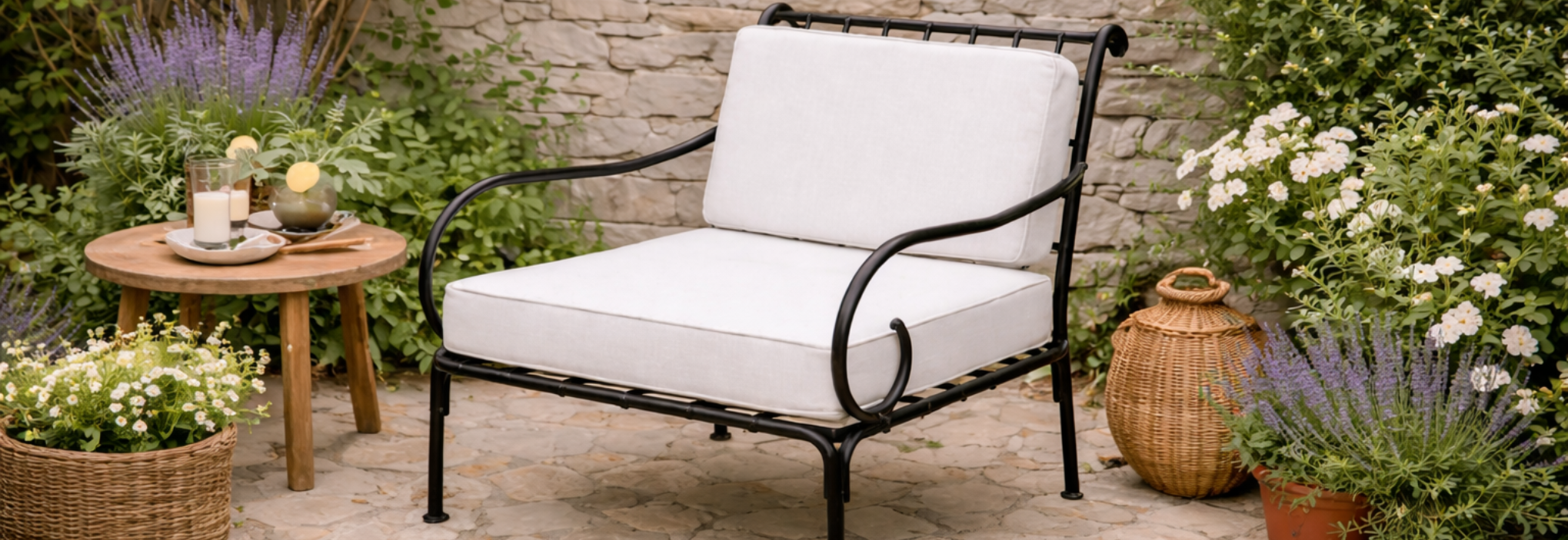 Fauteuil de jardin en fer forgé noir avec coussins blancs, installé sur terrasse en pierre naturelle dans un jardin fleuri au style méditerranéen.