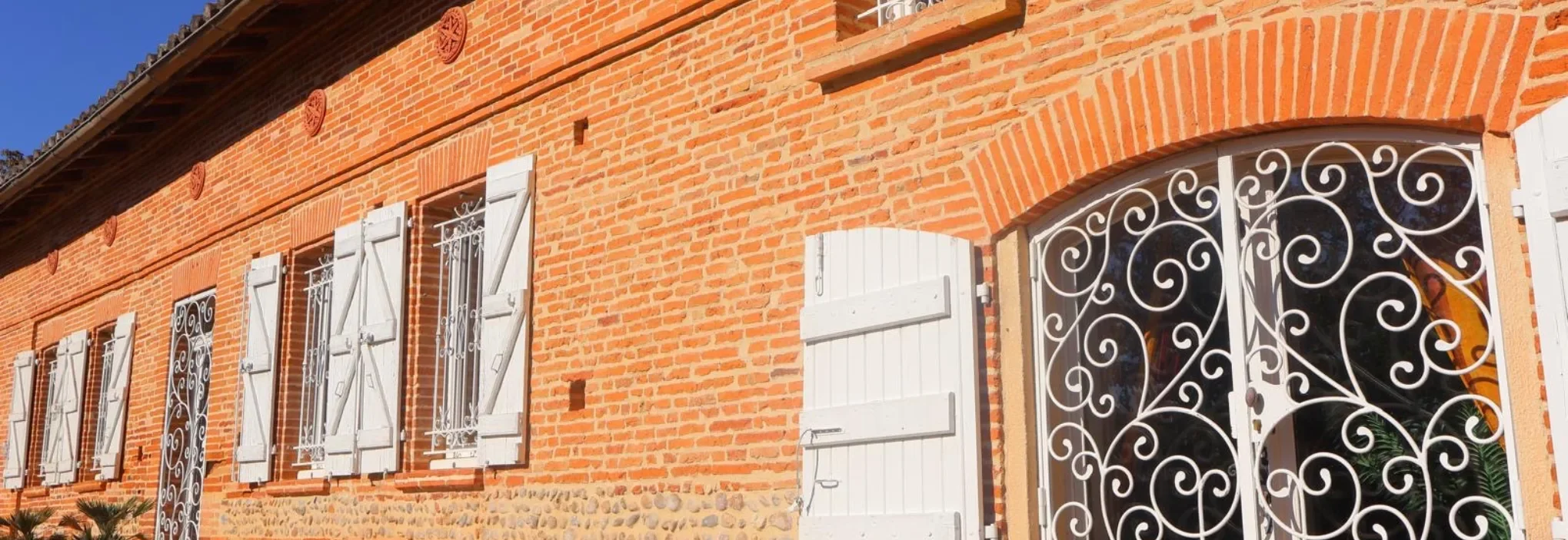 Façade en brique foraine avec volets blancs et ferronneries décoratives