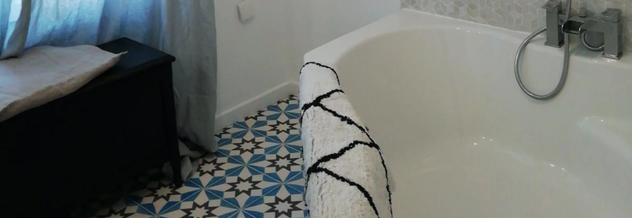 Salle de bain avec baignoire et sol en carreaux de ciment colorés, motif géométrique bleu et blanc
