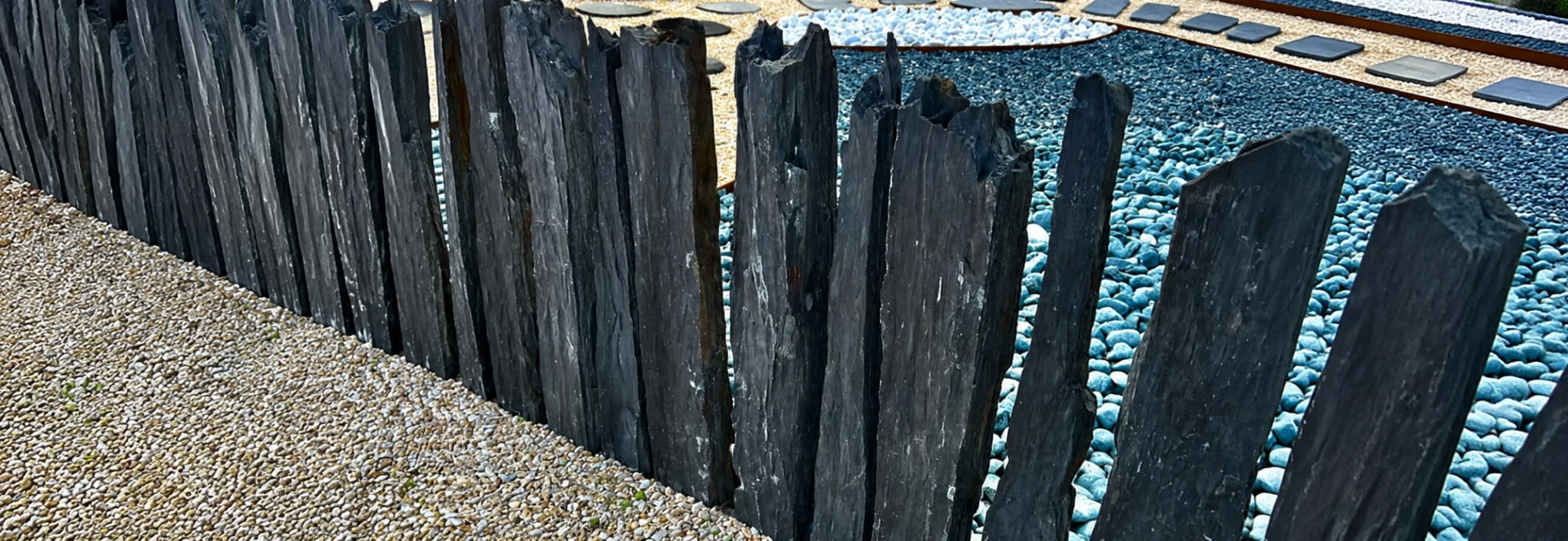 Piquets en schiste naturel noirs installés en bordure de jardin pour délimiter un espace paysager.