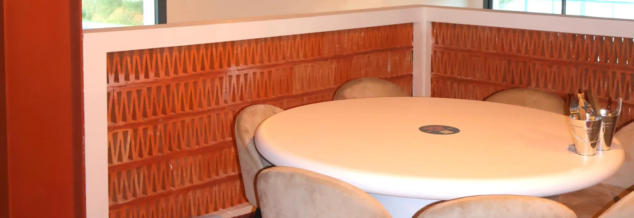 Claustra en terre cuite utilisé comme séparation murale dans un espace intérieur autour d’une table ronde.