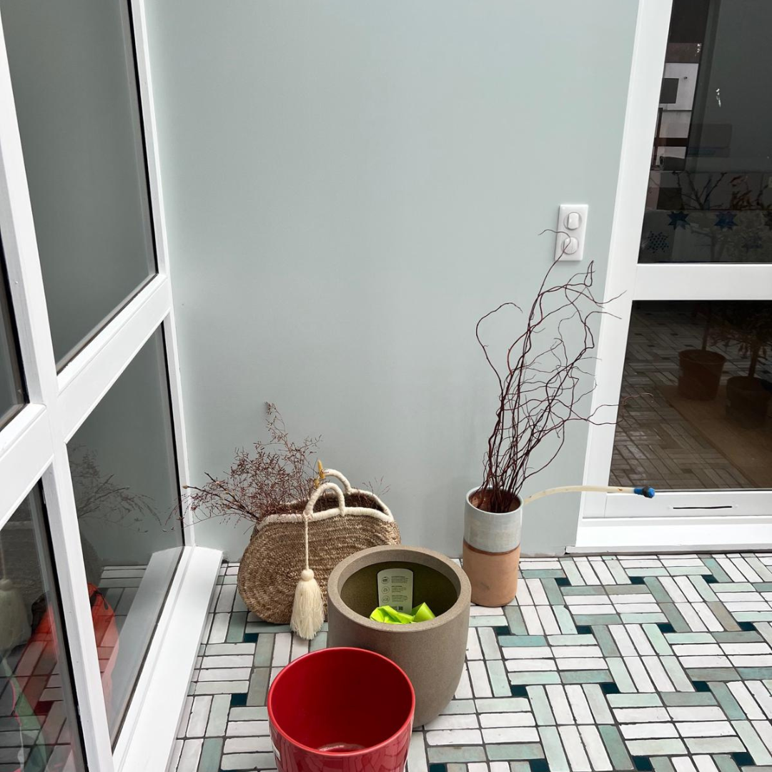 Sol en bejmat artisanal de Fès vert et blanc en terre cuite émaillée, formant un motif géométrique dans une véranda moderne avec paniers et pots de fleurs.