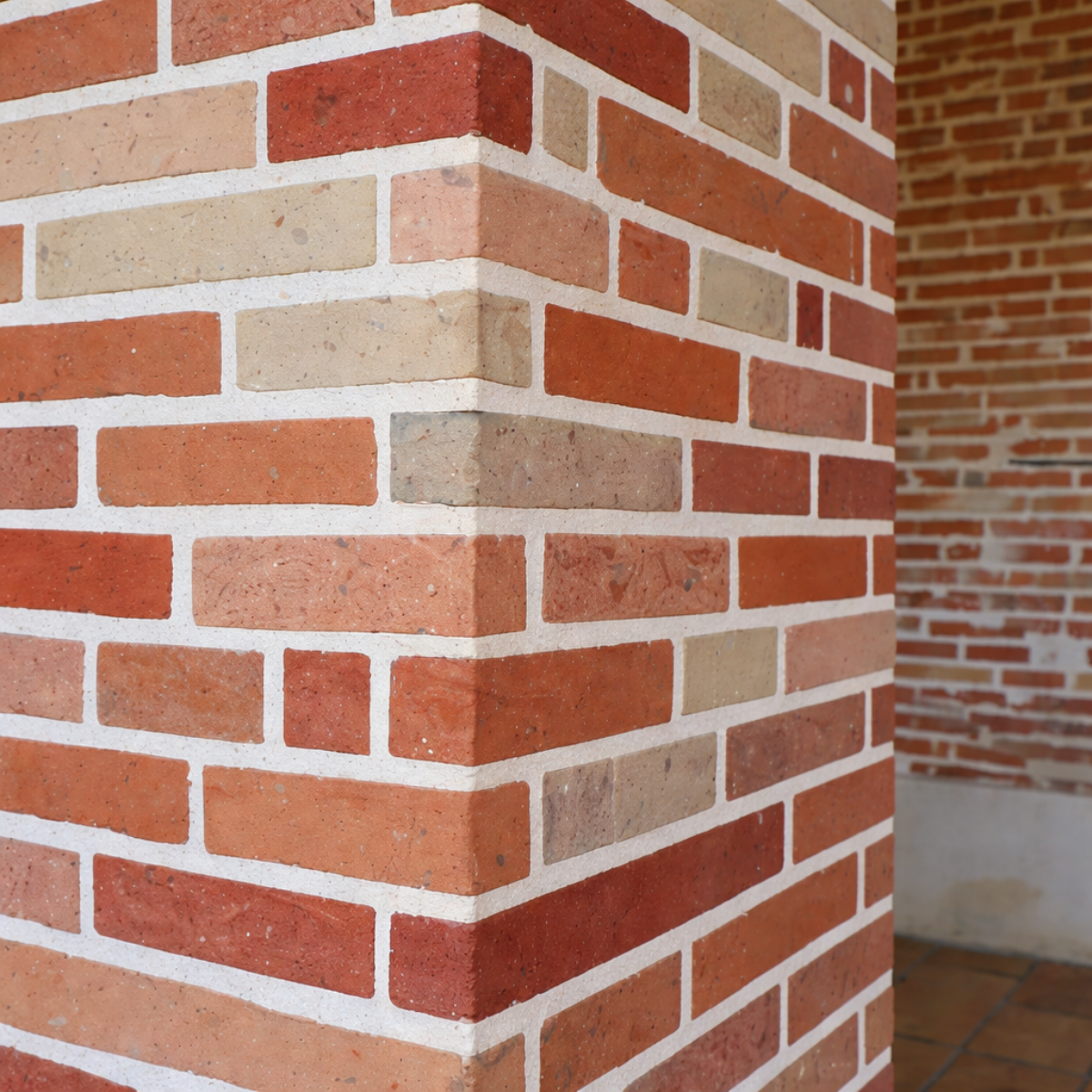 Chaise en fer forgé marron avec coussin beige sur une terrasse extérieure entourée de pots en terre cuite et de fleurs.
