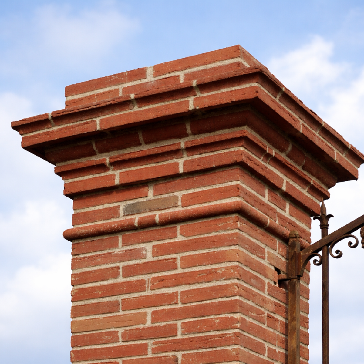 Chaise en fer forgé artisanale avec dossier arrondi et coussin beige, posée sur une terrasse fleurie en extérieur.