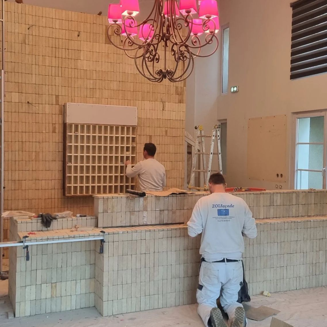 Pose de carreaux de bejmat beige artisanal de Fès sur un mur intérieur, réalisée par des artisans. Carrelage marocain en terre cuite naturelle dans une pièce lumineuse.