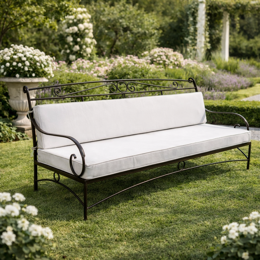 Chaise en fer forgé artisanale avec dossier arrondi et coussin beige, posée sur une terrasse fleurie en extérieur.